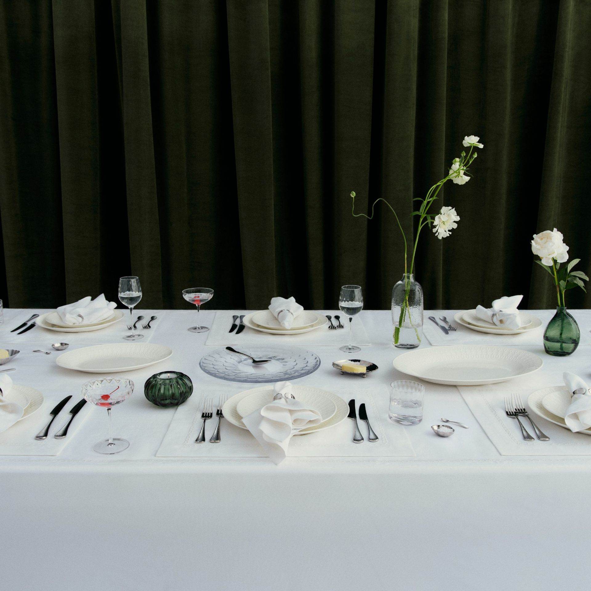A dining table set with ictoria Beckham's tableware from her collection with Westwing set against a dark green velvet curtain