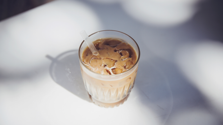 Iced coffee in a glass with a straw on a sun-dappled counter