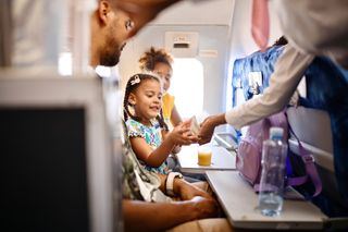 child interacting with air hostess on a plane. The seat trays are down with drinks on them