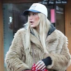 Bella Hadid wearing a fur coat, baseball cap, red triangle scarf, leggings, and Ugg Classic Tall Boots in Aspen