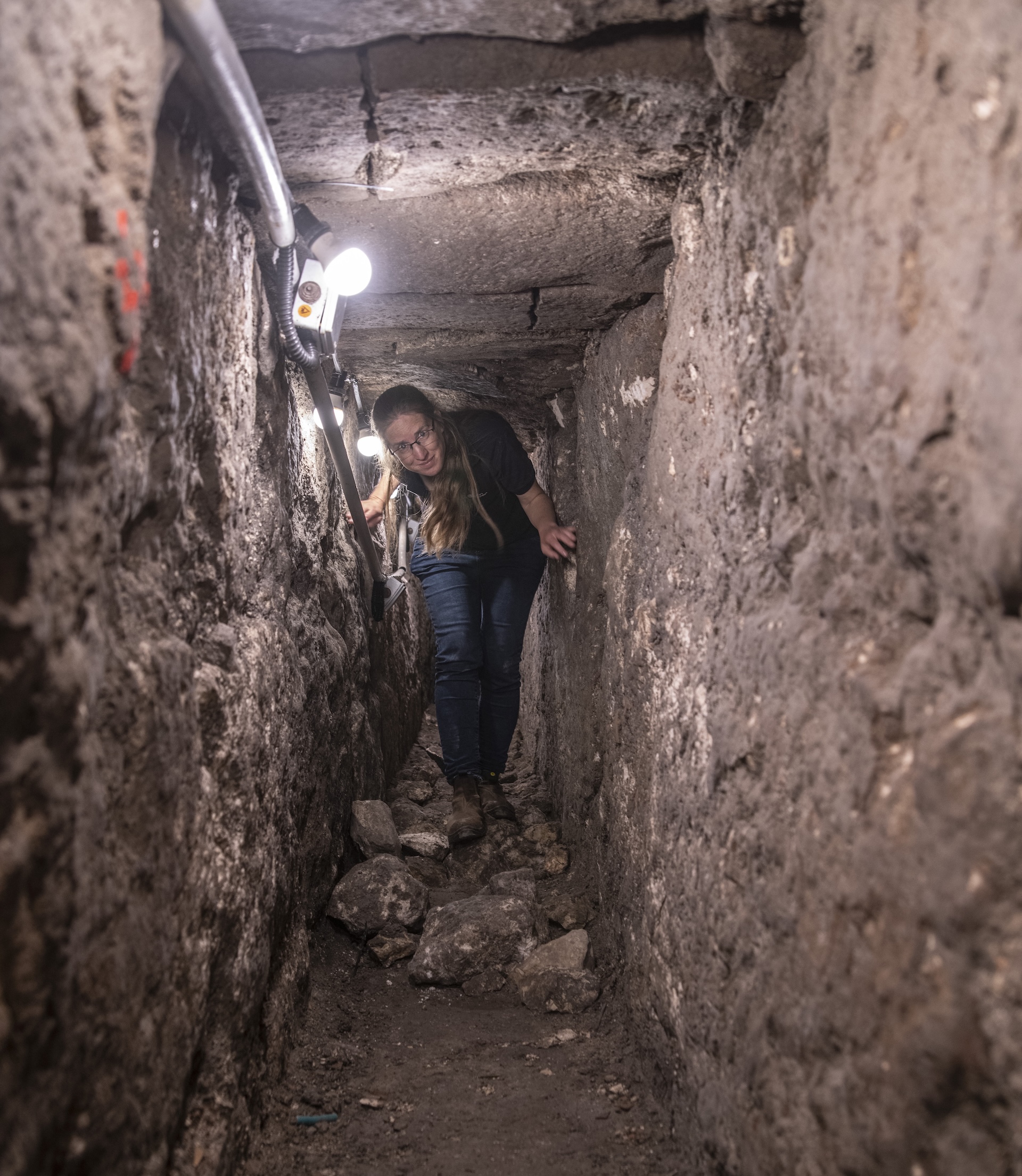 a woman walks through a narrow stone tunnel