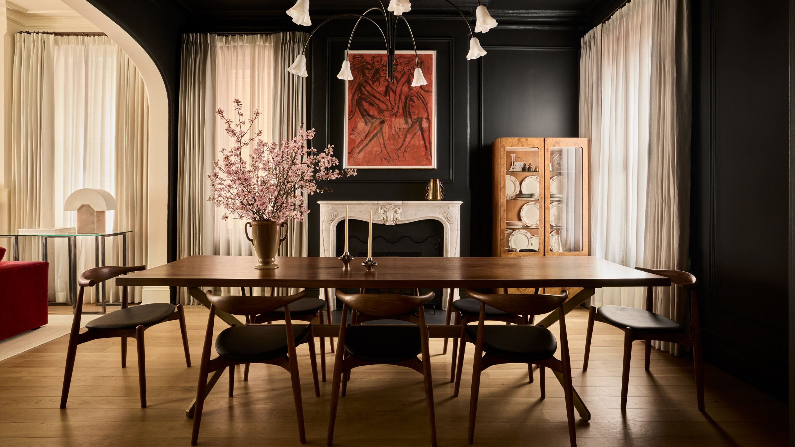 a dark black painted dining room with antique fireplace styled with contemporary art and mid century furniture