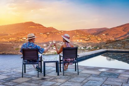An elderly couple retire abroad and enjoy the summer sunset with a glass of wine