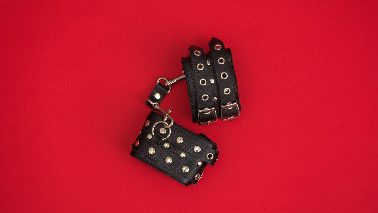 leather handcuffs on red background for BDSM for beginners 