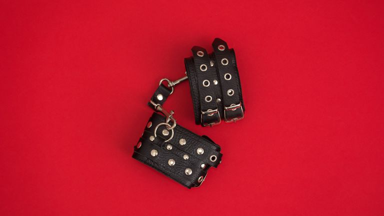 leather handcuffs on red background for BDSM for beginners