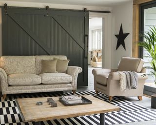 A modern farmhouse living room with green barn doors, cream sofa furniture and monochrome black and white rug