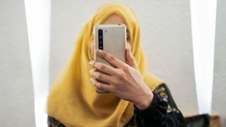 Afghan woman with her face obscured by her phone in the hand