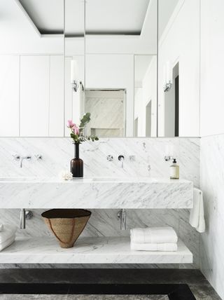 A double white marble vanity with folded white towels on the shelving