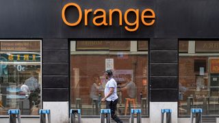 Pedestrian walks past Orange store front with logo and branding picture on building facade.