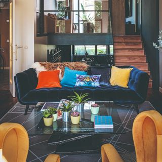 An open-plan living room with a curved pin-tucked blue velvet sofa and contrasting scatter cushions