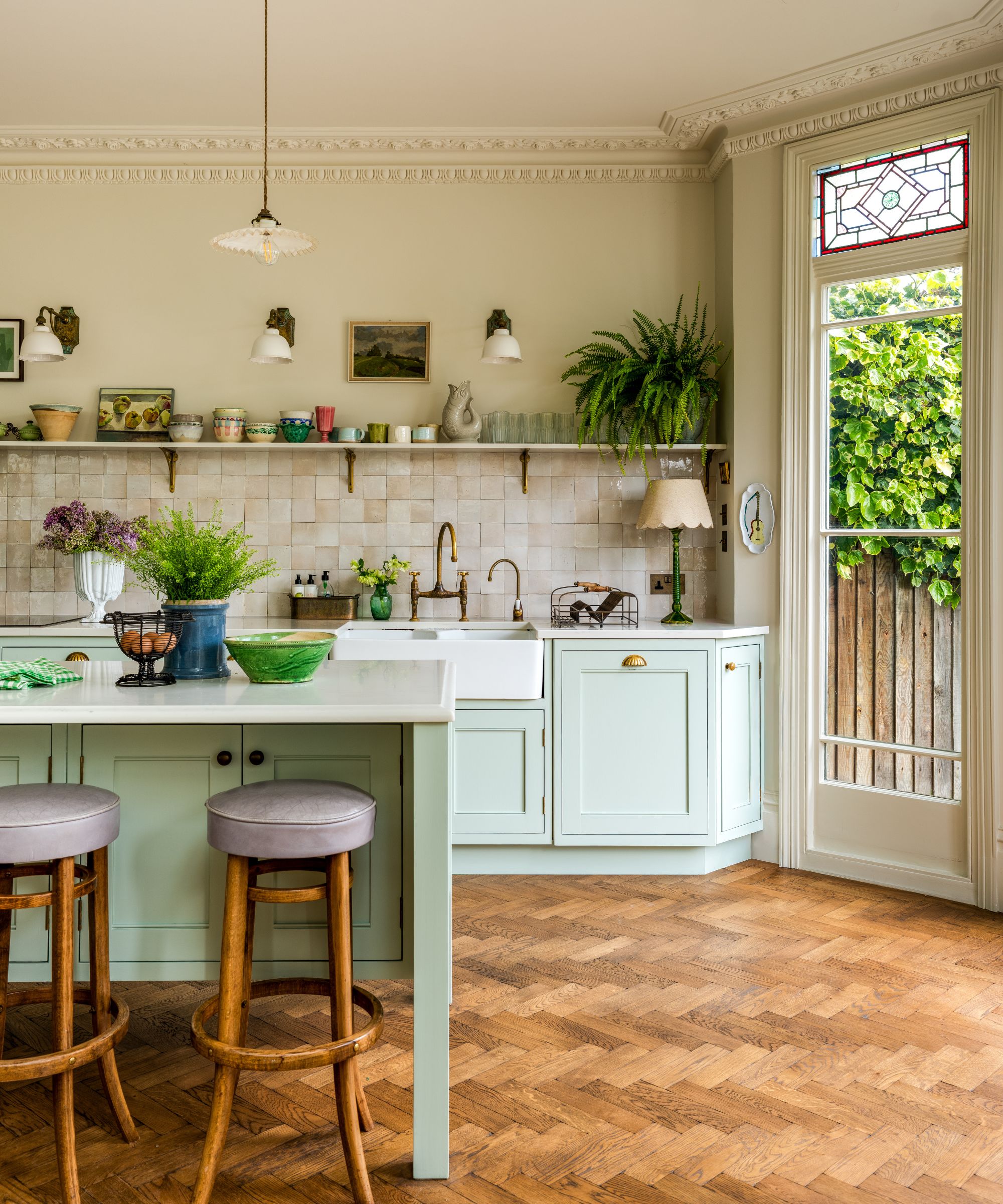 A large kitchen with light blue cabinets, white countertops, a tiled backsplash, wooden floors, and stained glass windows