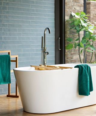 Bathroom with blue subway tiles, green towels and white freestanding bath