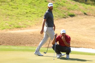 Brooks Koepka lines up his putt whilst Dustin Johnson walks past him