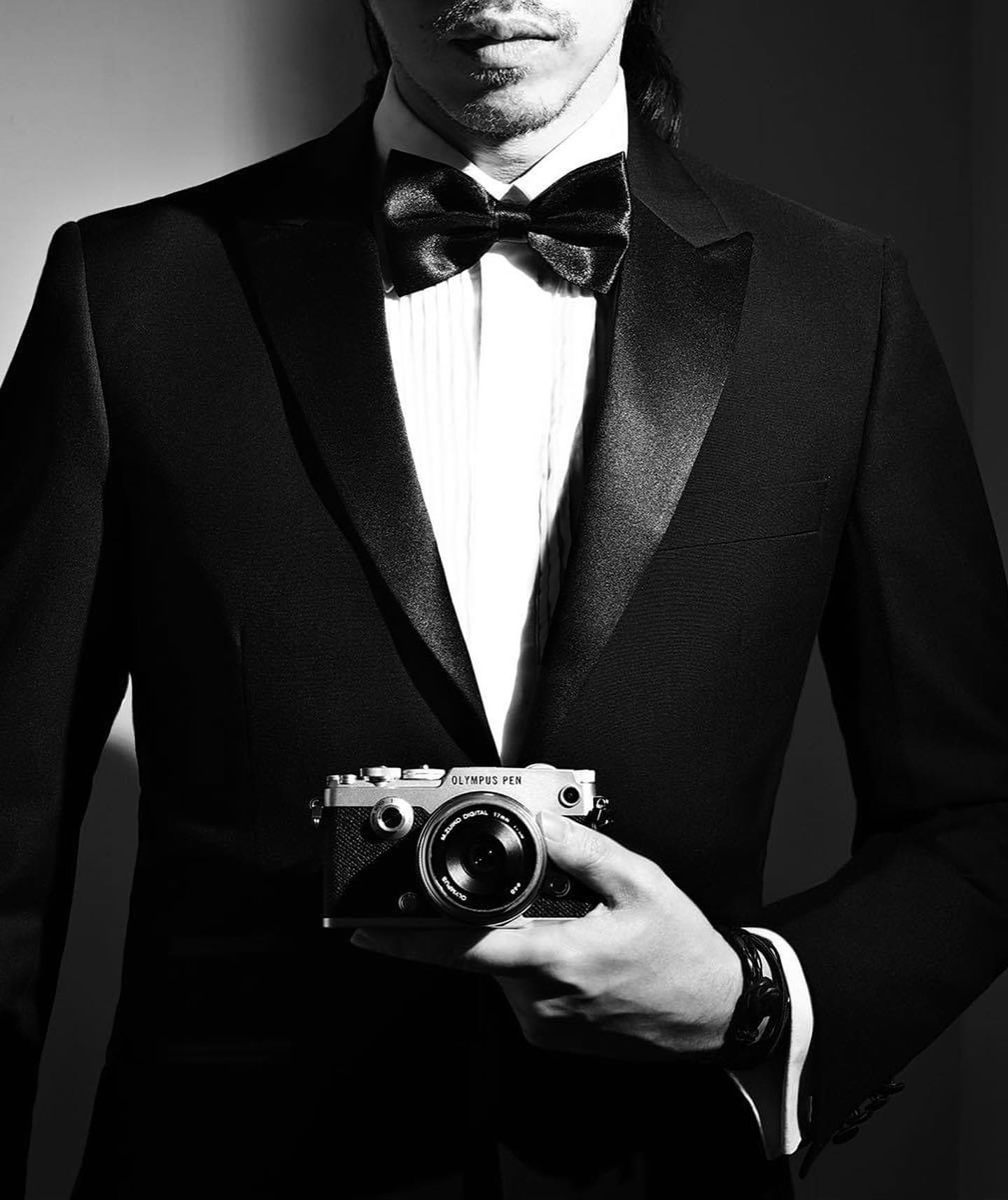 Photographer James Artaius, wearing a tuxedo, holding an Olympus PEN-F (2016)