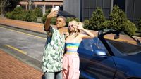 Inzoi - two characters pose for a selfie together in front of a blue convertible car