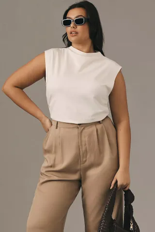 model wears white mock neck shell and tan pants