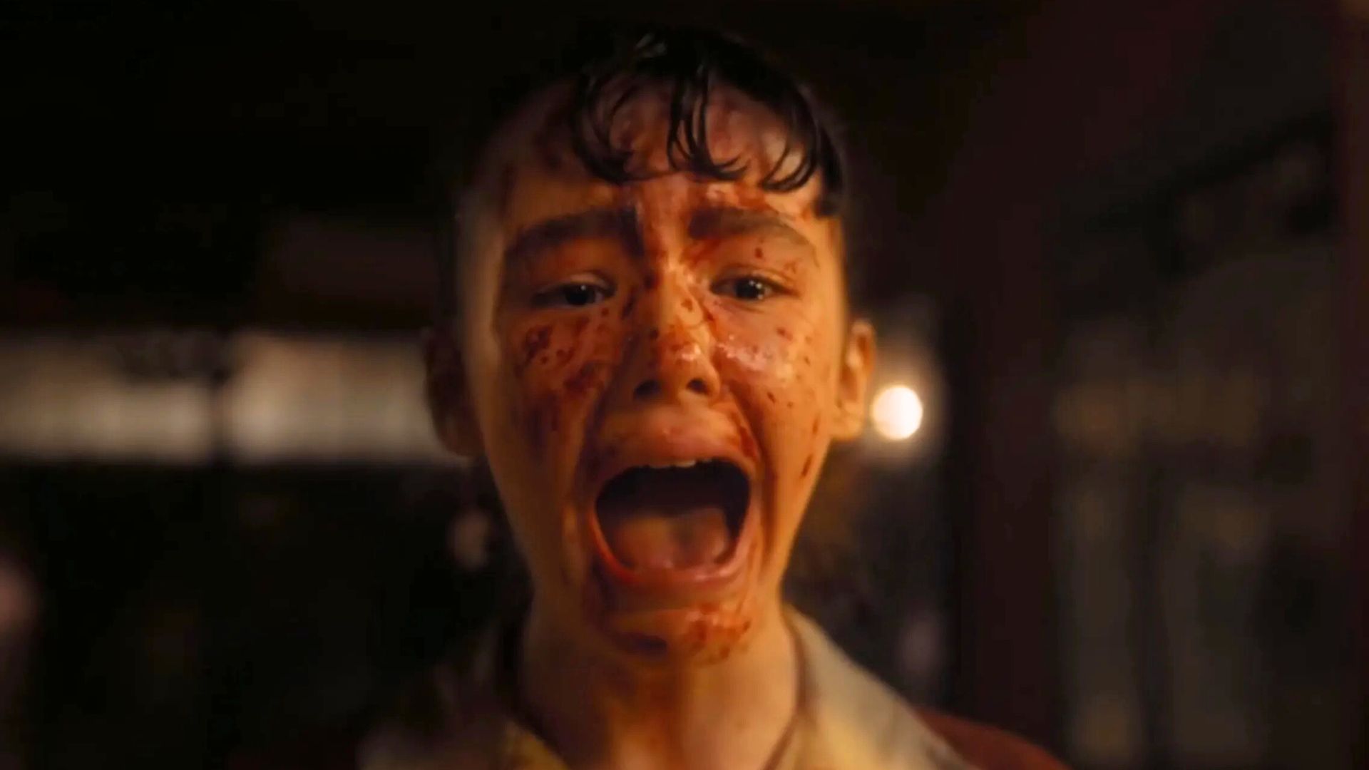 A child with a blood-spattered face screams at something offscreen