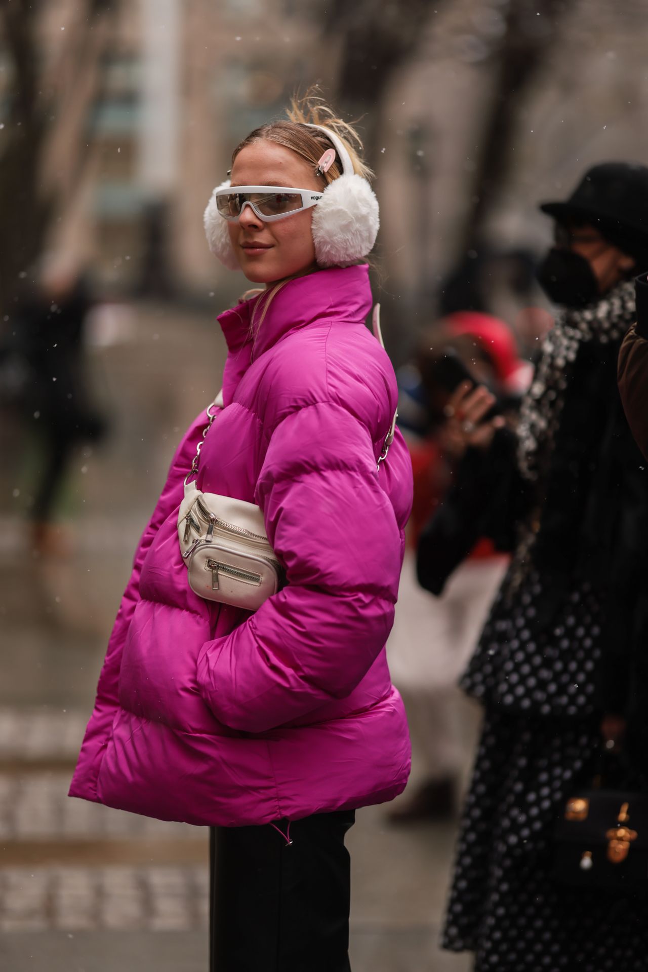 NEW YORK, NEW YORK - FEBRUARY 13: A guest wears a pink shiny oversized high neck puffer jacket, black shiny leather large pants, a white leather fanny pack bag, outside Ulla Johnson, during New York Fashion Week on February 13, 2022 in New York City. (Photo by Jeremy Moeller/Getty Images)