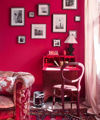 Hot pink living room with monochromatic gallery wall, red vintage rug, dark pink desk and chair, vintage floral couch