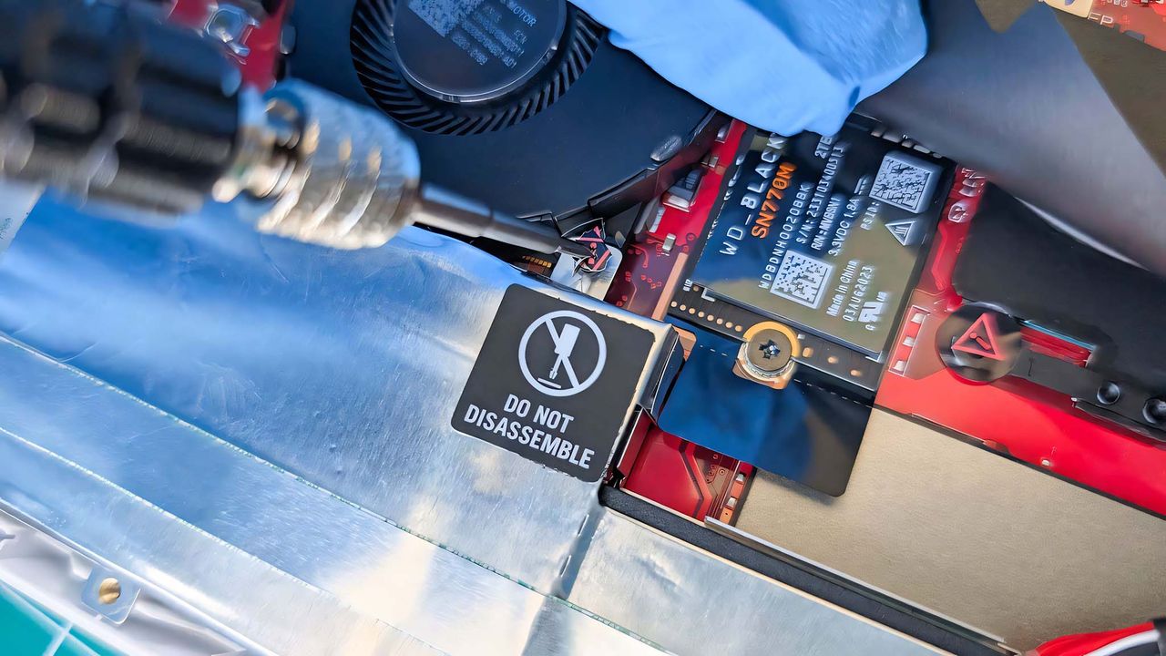 A screwdriver unscrewing a screw inside ROG Ally that has a warning sticker on top of it.