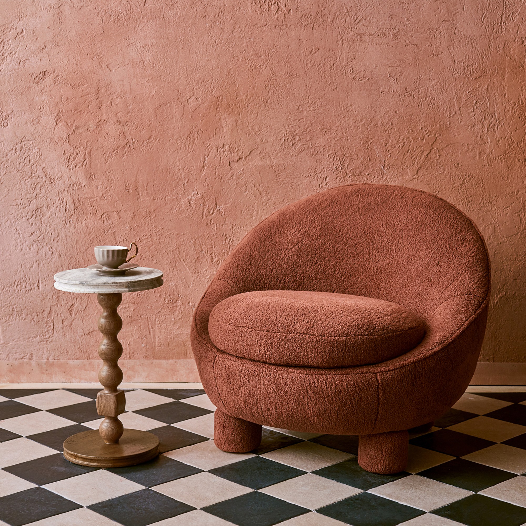 The Rumi chair from Tan France's collection for Castlery in pink with a side table set against a pink plastered wall and black and white chequered floor