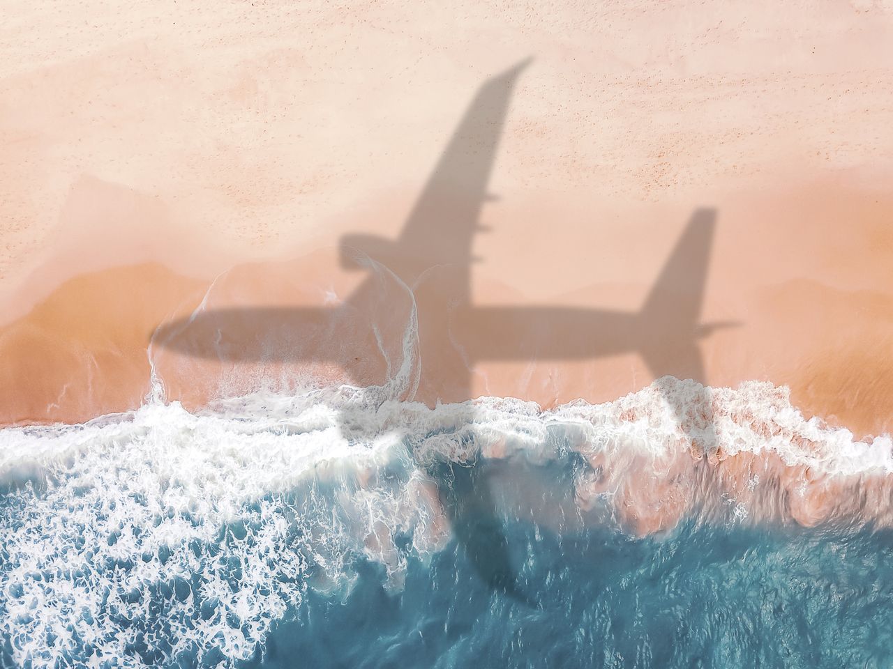 Shadow of a flying aeroplane, cast over an idyllic beach scene