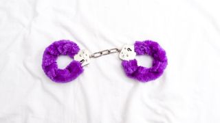Purple fluffy handcuffs on white bedsheets