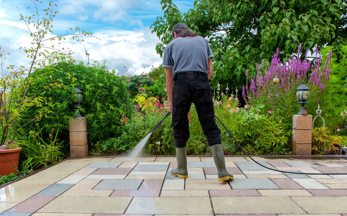 Image shows a man pressure washing a patio.