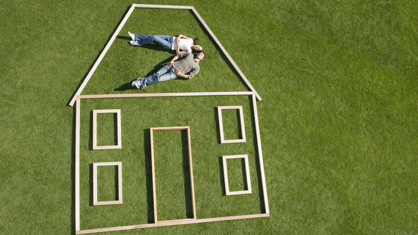 house outline made from pieces of wood on large area of grass with couple lying on floor in roof section