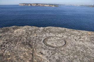 Inscriptions carved near the edge of a cliff with Sydney's skyline in the distance.