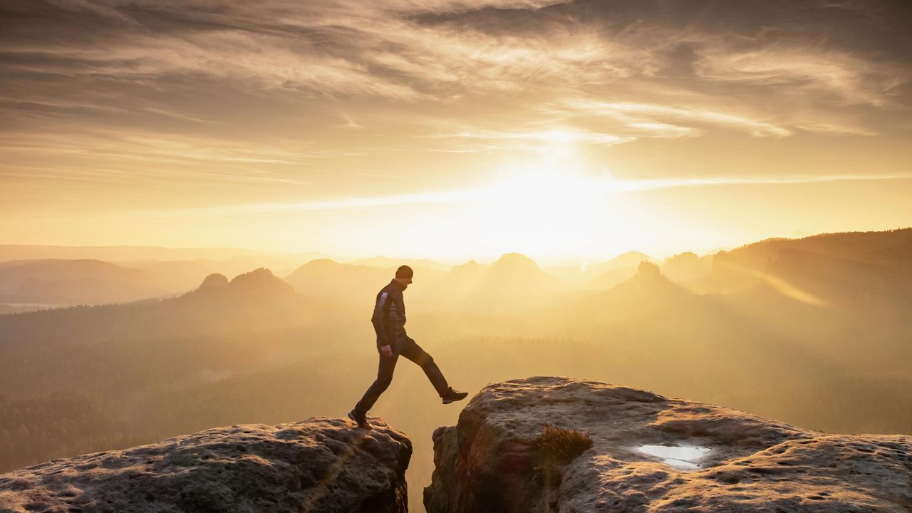 A man gingerly steps across a crevice while hiking.