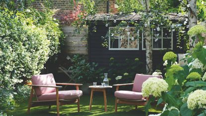 Garden with bushes and trees on either side and seating area in the middle