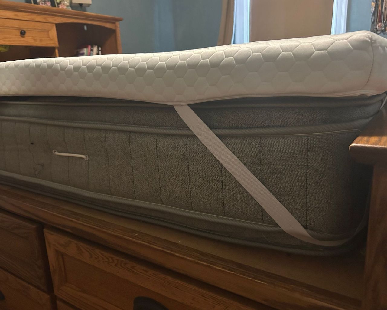 Corner of the white Helix ErgoAlign Mattress Topper on a gray mattress on a wooden bedframe.