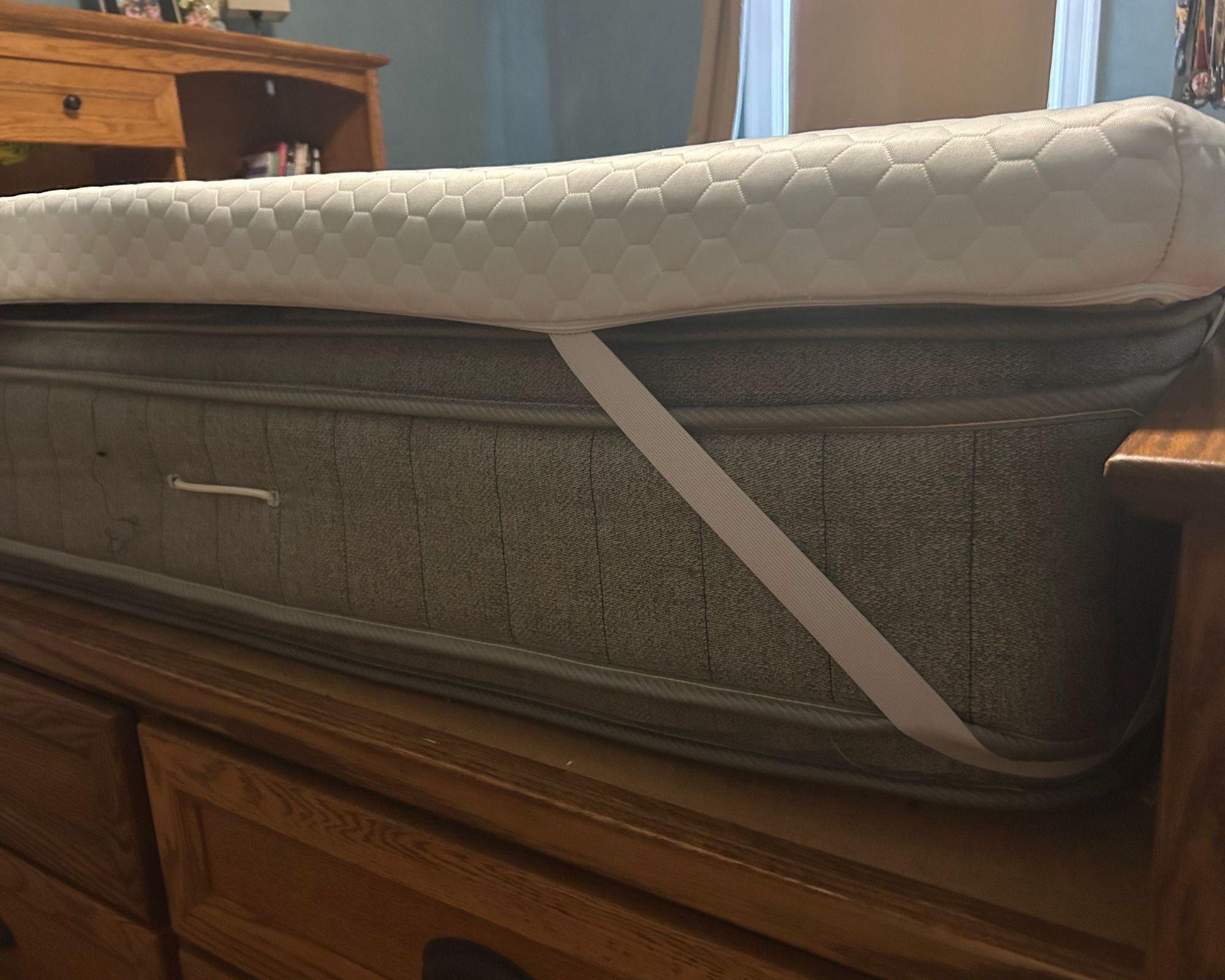 Corner of the white Helix ErgoAlign Mattress Topper on a gray mattress on a wooden bedframe.