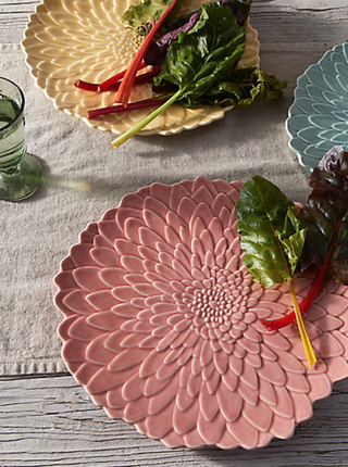 three large serving plates with intricate floral textured detail laid flat on a table with salad leaves on top