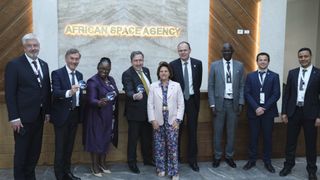 nine people in business attire smile and pose for a portrait in front of a sign that reads "african space agency"