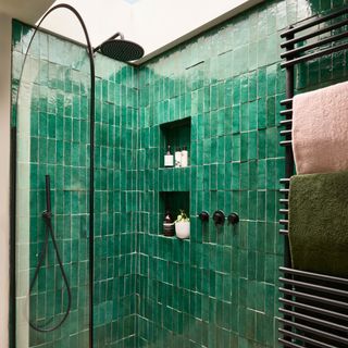 a shower area with emerald green tiles a clear glass shower panel with curved top and black hardware