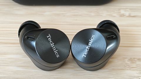 A pair of wireless Panasonic Technics EAH-AZ60M2 earbuds and a charging case on a wooden desk