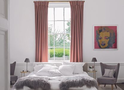A bedroom with a bed placed in front of a window with pink drapes 