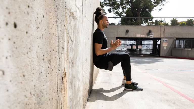 Man performs a wall sit using a wall outside