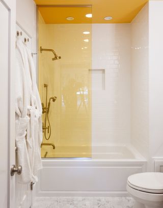 A bathroom with a yellow shower partition, and a shower nook with ceiling lights