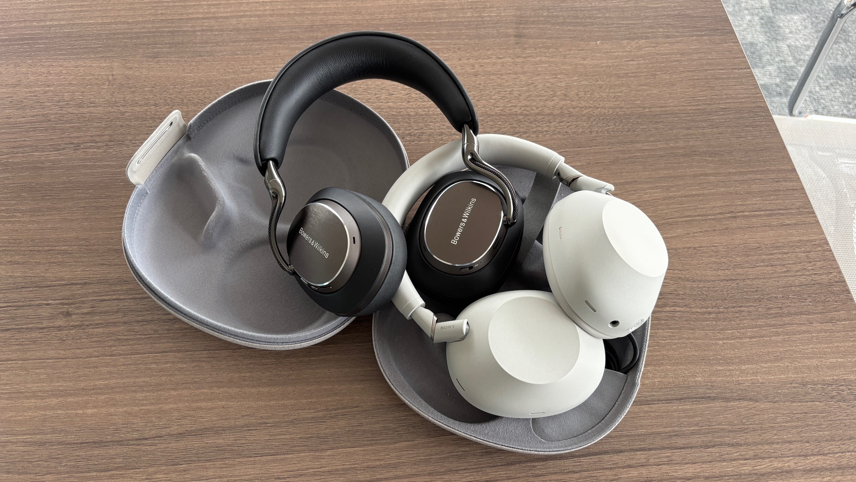 Bowers &amp;amp; Wilkins Px8 S2 and Sony WH-1000XM6 headphones in their carry cases on a wooden table.