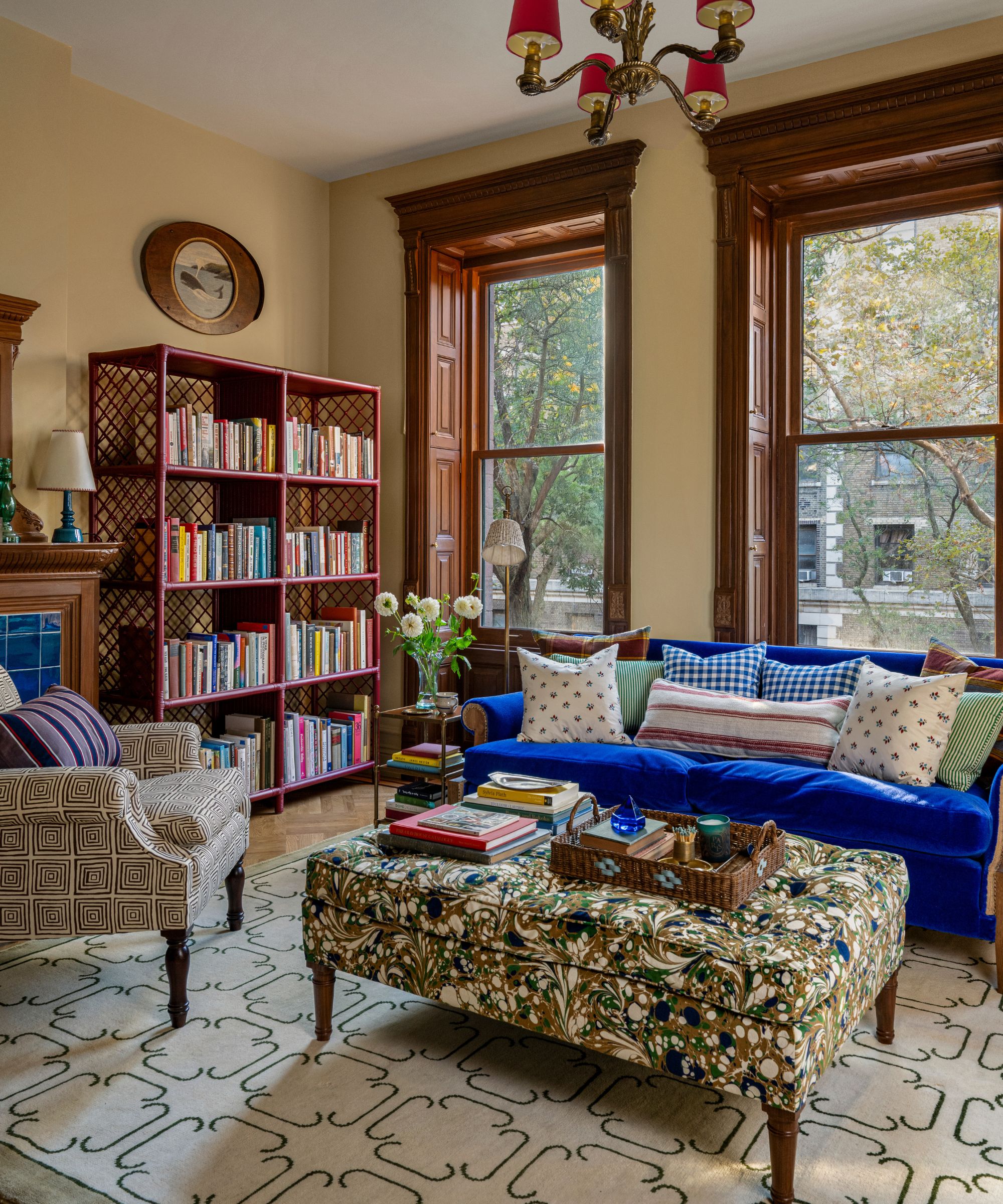 a brownstone home library with yellow walls and tall original wooden casement window, a blue velvet couch and a bookcase