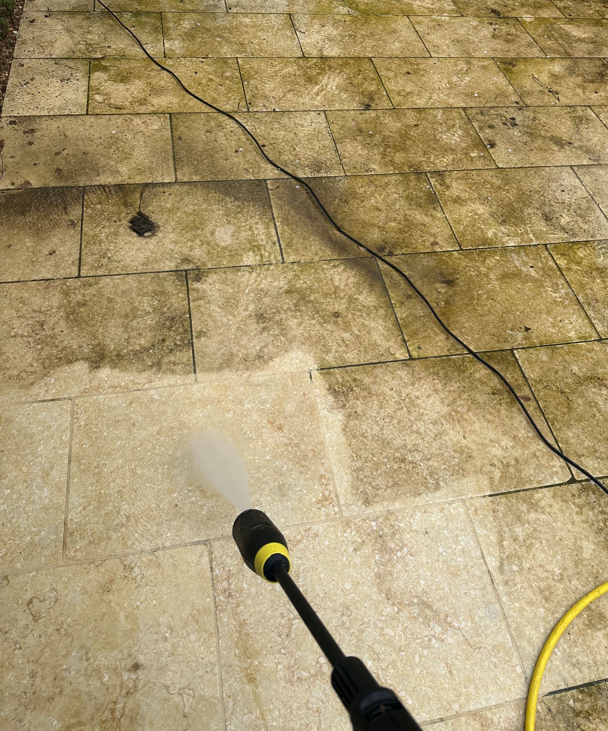 A yellow K&auml;rcher K5 Comfort Premium pressure washer on a cream limestone patio