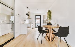 light wood flooring laid in white kitchen with wooden table and black chairs