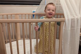 Our tester's little boy standing and smiling in the Stokkee Sleepi cot bed during testing