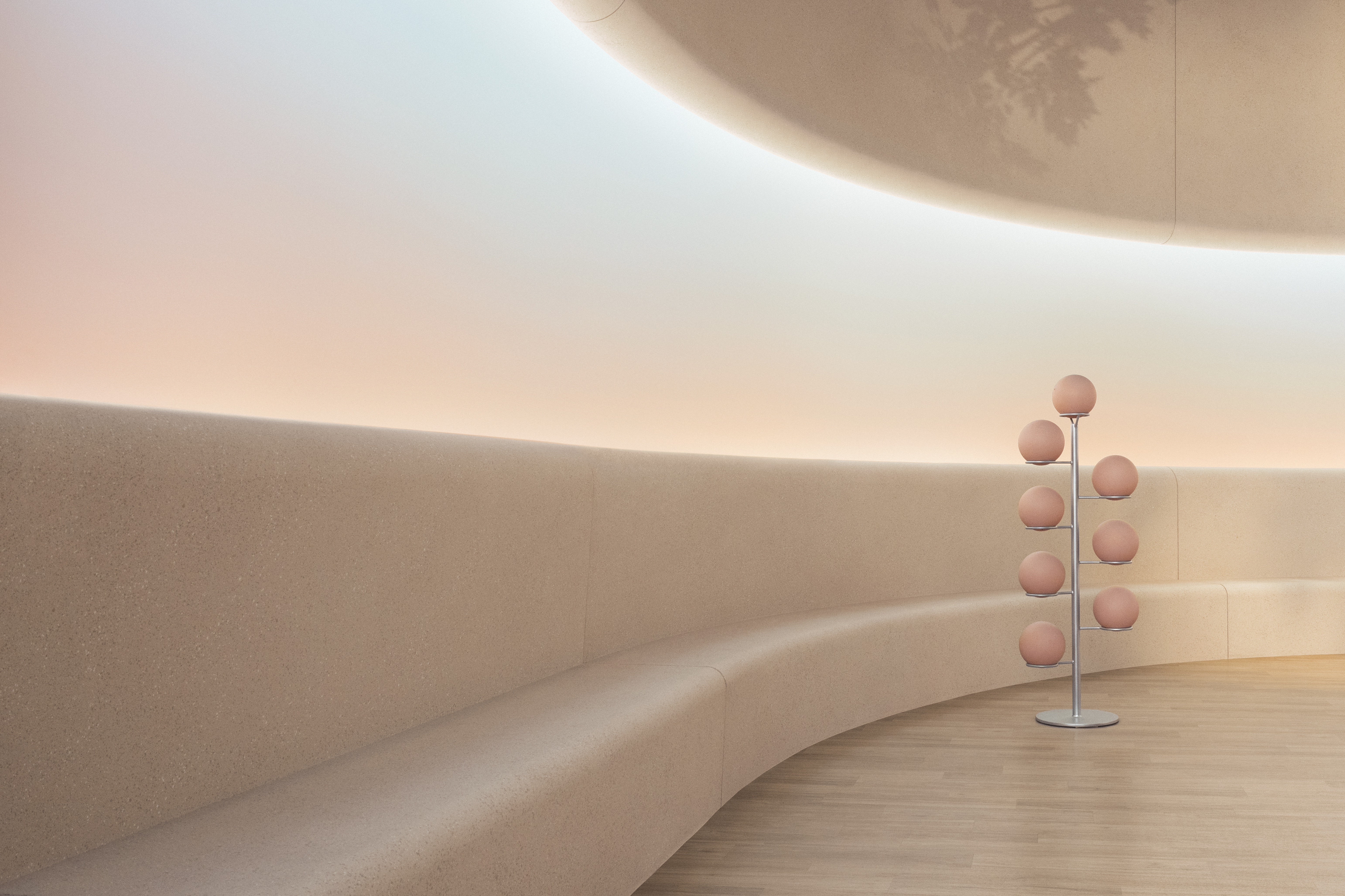 A skin-toned room with gradient light going from water green to pink showcases a series of artistically designed spherical weights stacked on a chrome rail and a soft, all-encompassing upholstered banquette.