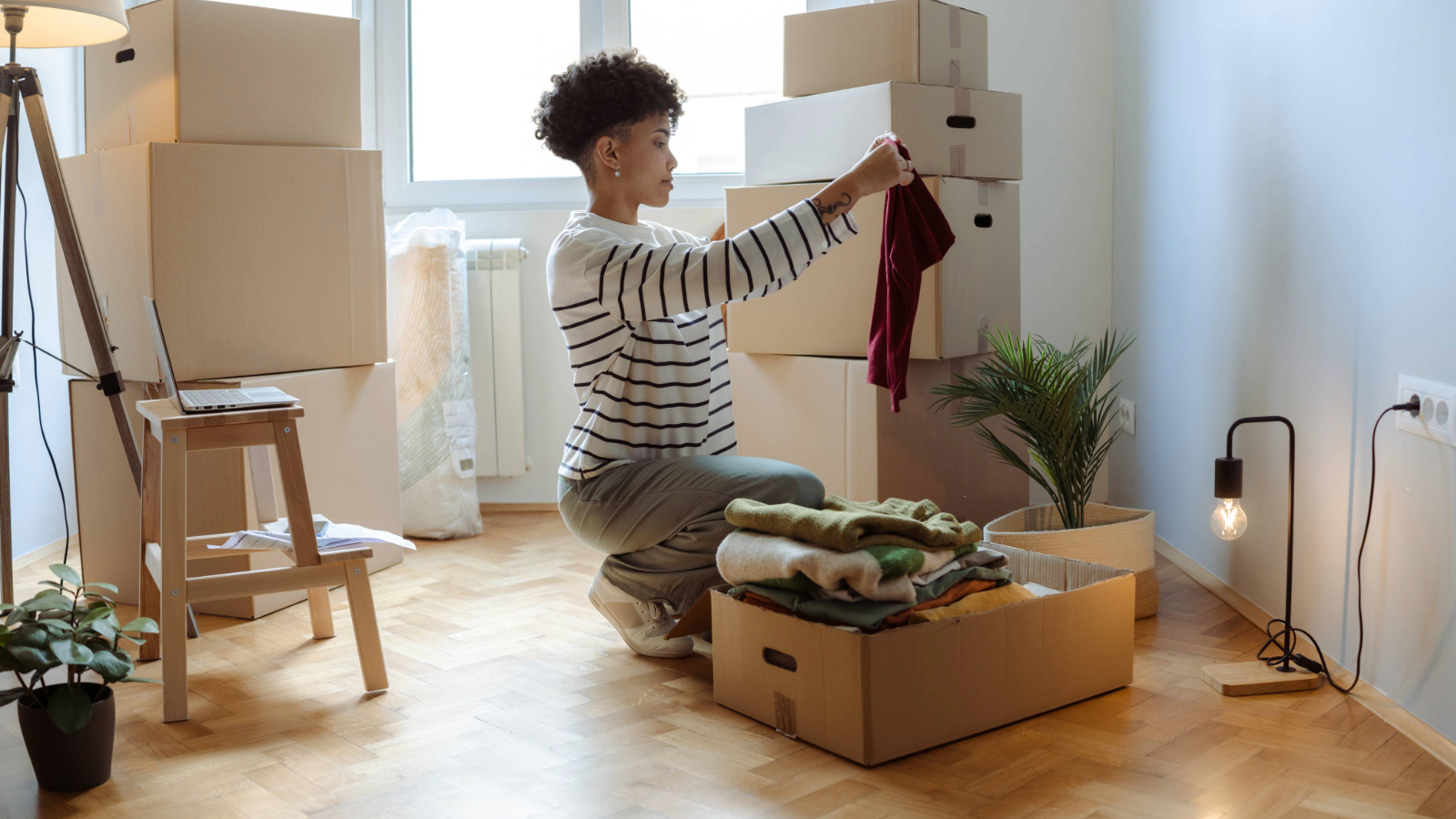 Woman holding up an item of clothing surrounded by stacked cardboard boxes