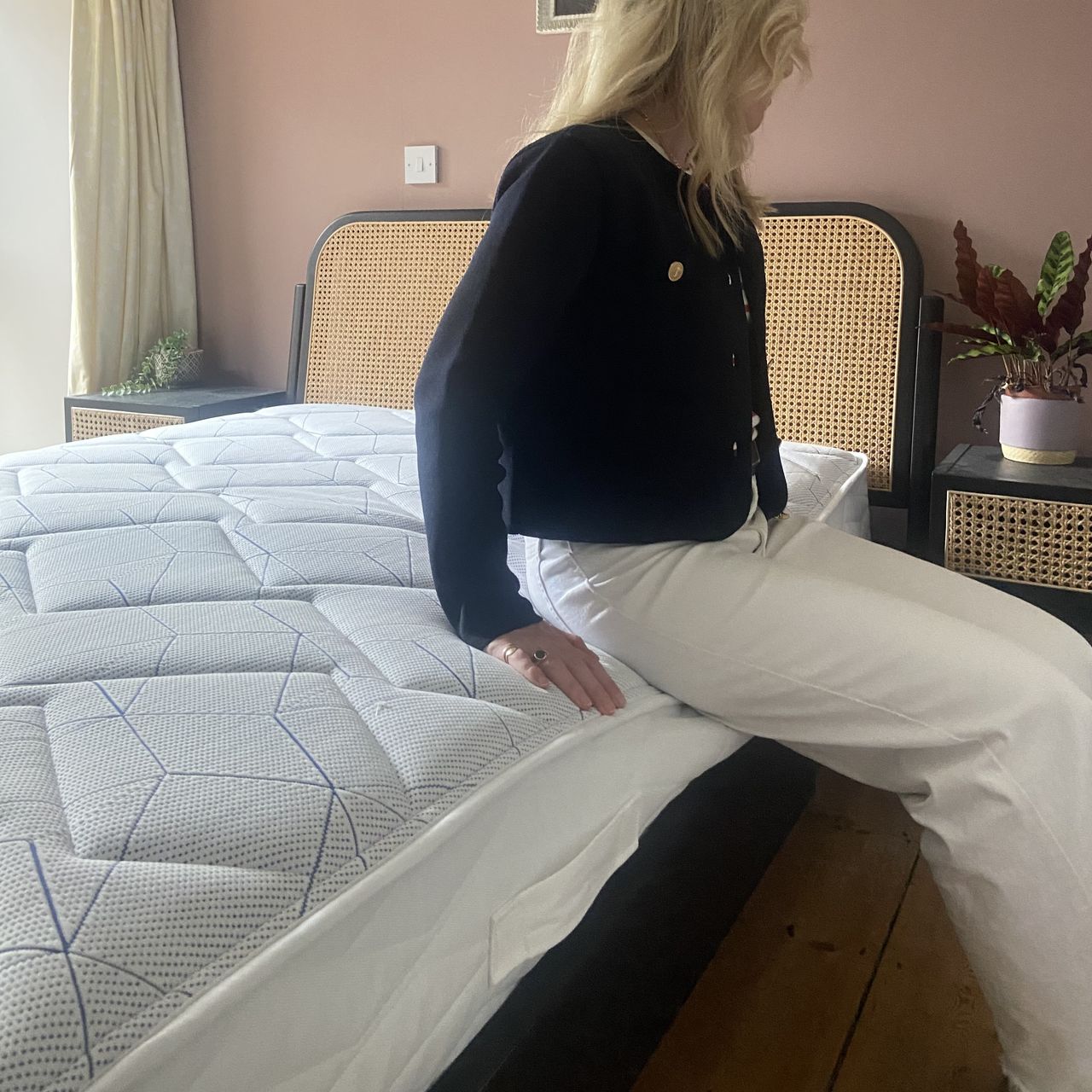 A woman in a black top and white trousers sitting on the edge of the Bensons for Beds Simply Support Pocket Sprung Mattress.
