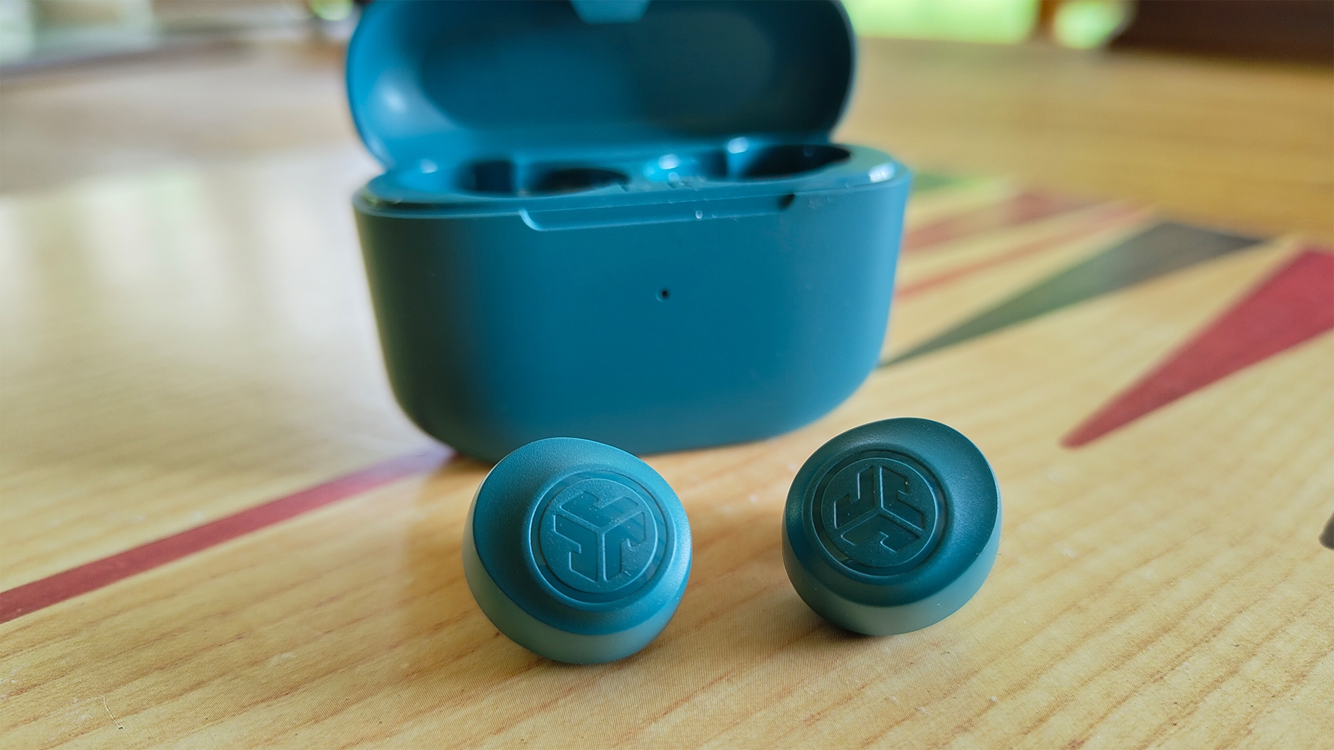 JLab Go Pop+ in-ear headphones on wooden surface in front of open charging case